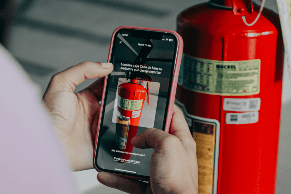 mulher segurando um celular para abrir um chamado de manutenção de um extintor de incêndio usando o Trílogo, um sistema de inventário patrimonial